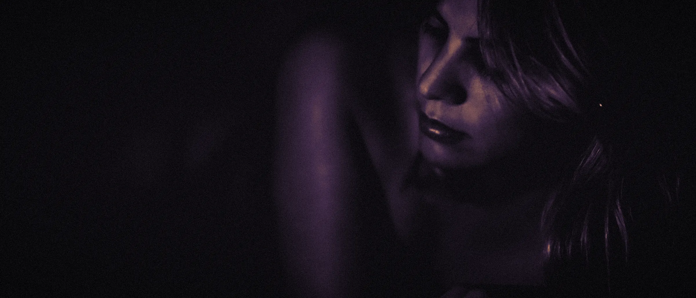 A woman resting her head on her arm in a dark room, lit softly from the side